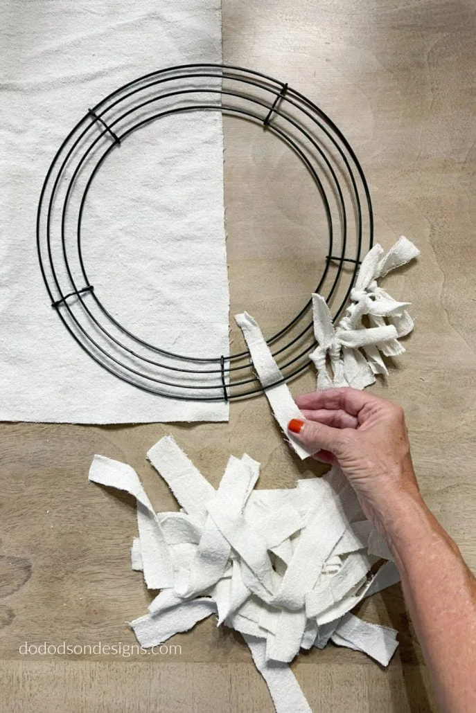 Hands tying fabric strips onto a wire wreath frame
